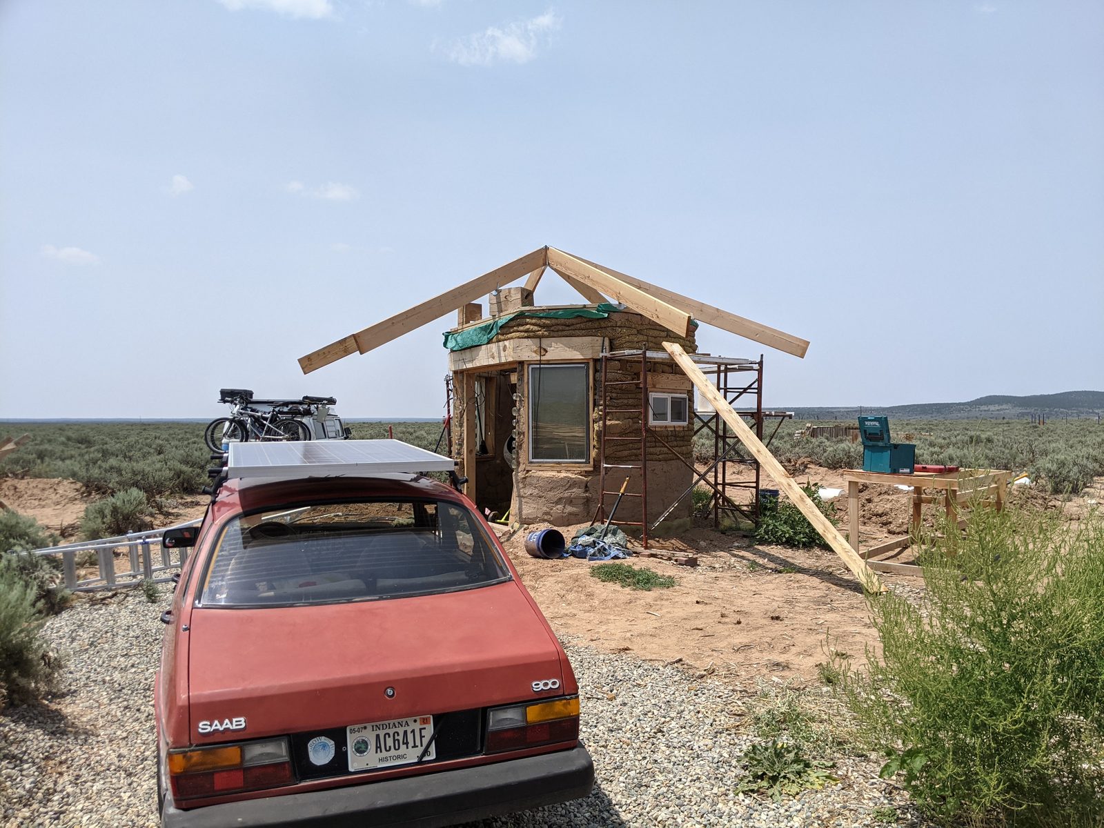 Build site in the high desert: timber roof framing above earthen walls under a wide sky